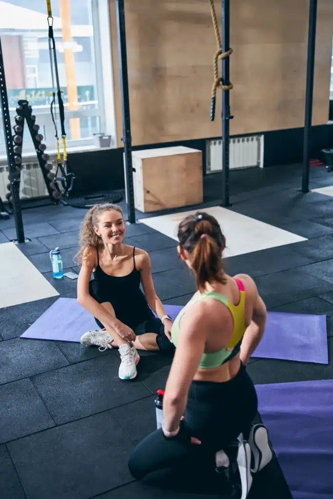 Deux femmes discutant après une séance de coaching personnalisé sur tapis, partageant des conseils de remise en forme.