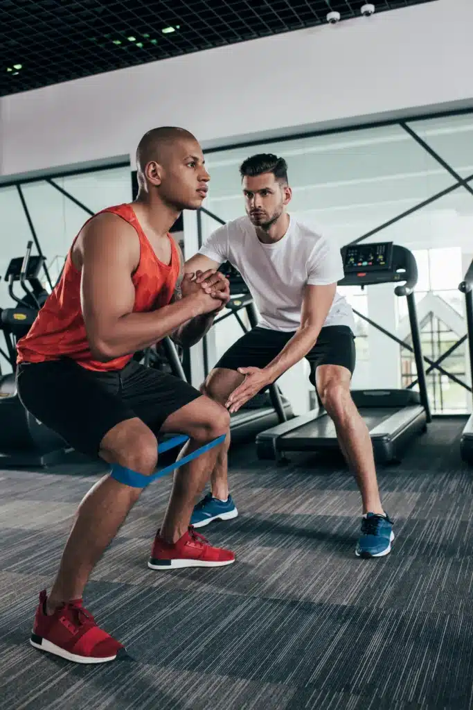 Coach aidant un homme à réaliser des squats avec une bande élastique lors d'une séance de coaching personnalisé.