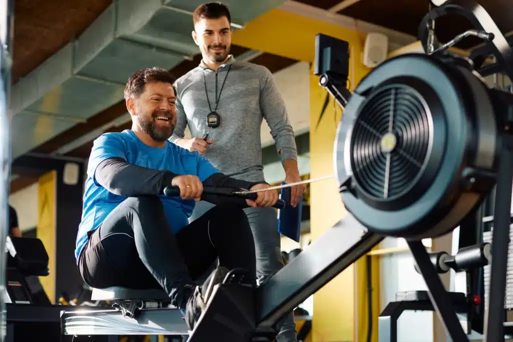 Coach encourageant un homme sur un rameur pendant une séance de coaching personnalisé pour améliorer l'endurance et la force.