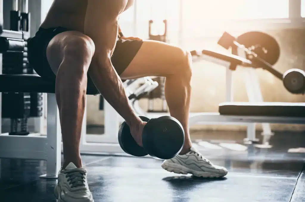 Homme soulevant des haltères lors d'un cours de fitness, se concentrant sur le renforcement musculaire dans une salle de sport bien équipée.