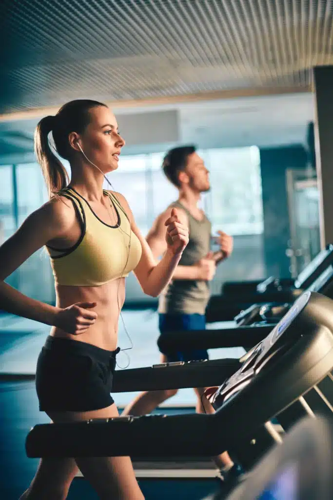 Homme et femme courant sur des tapis de course lors d'un cours de fitness, axé sur le cardio pour améliorer l'endurance et la santé cardiovasculaire.