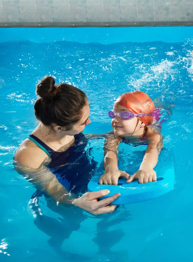 Instructrice aidant un enfant à nager avec une planche lors d'un cours de sport aquatique, favorisant l'apprentissage de la natation.