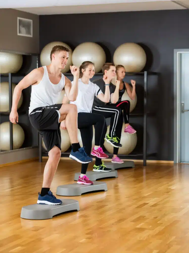 Participants pratiquant des exercices de step lors d'un cours de sport en salle, visant à améliorer la coordination et la condition physique.