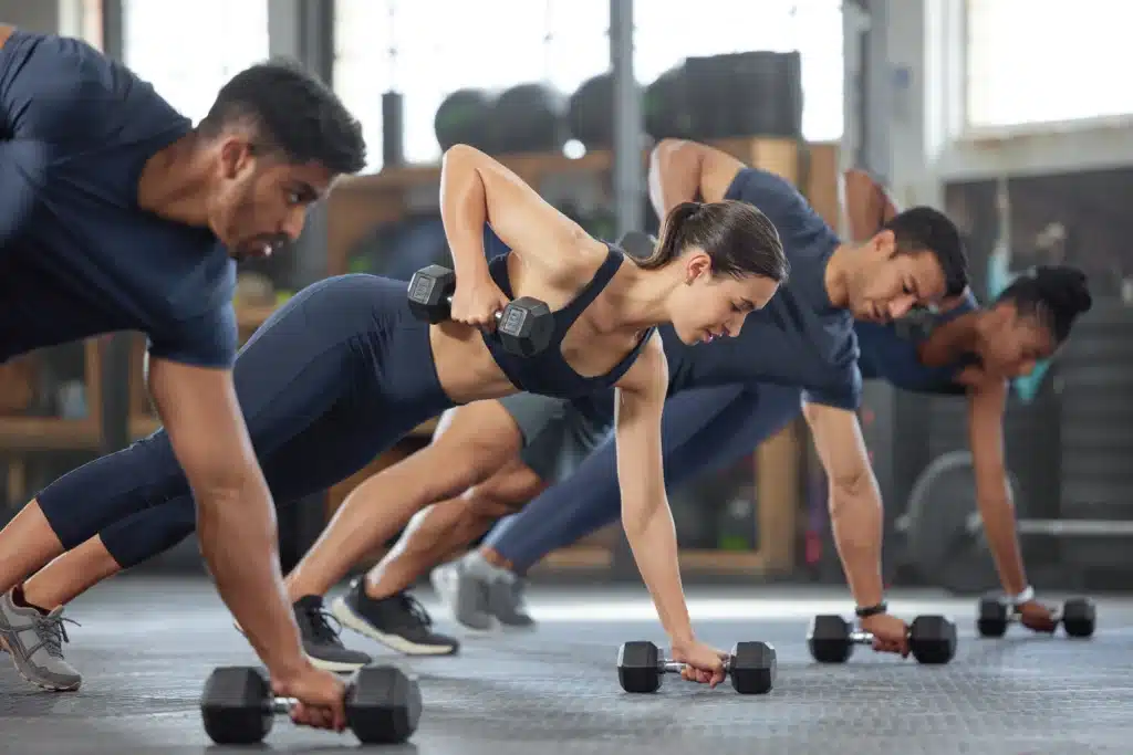 Groupe de personnes réalisant des exercices avec des haltères lors d'un cours de sport, mettant l'accent sur la force et l'endurance.