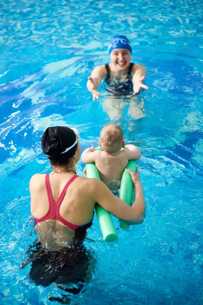 Bébé accompagné par ses parents et une instructrice pendant un cours de natation, introduisant les tout-petits au plaisir de l'eau.