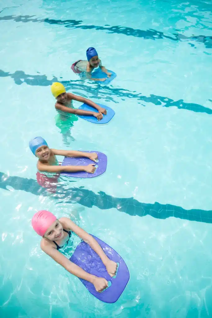 Groupe d'enfants pratiquant la natation avec des planches lors d'un cours de natation collectif, renforçant leur aisance aquatique.